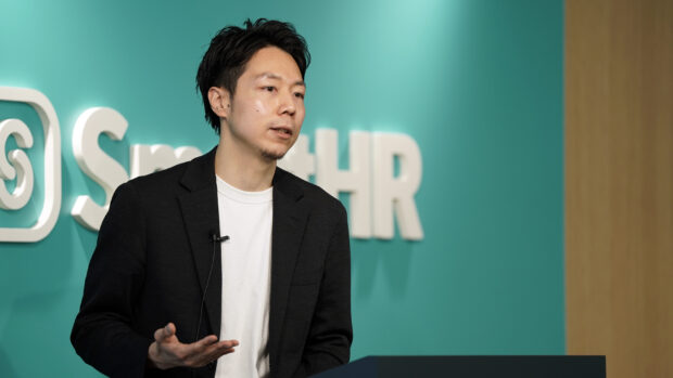 SmartHRのロゴを背景に登壇する代表取締役CEO芹澤のバストアップ写真